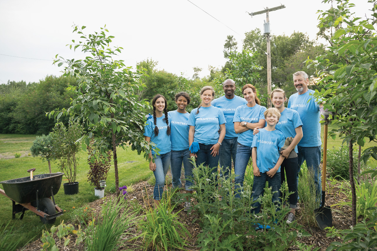 Group of diverse people outside in blue volunteer t-shirts working on environmental clean up and reads creating a sustainable future