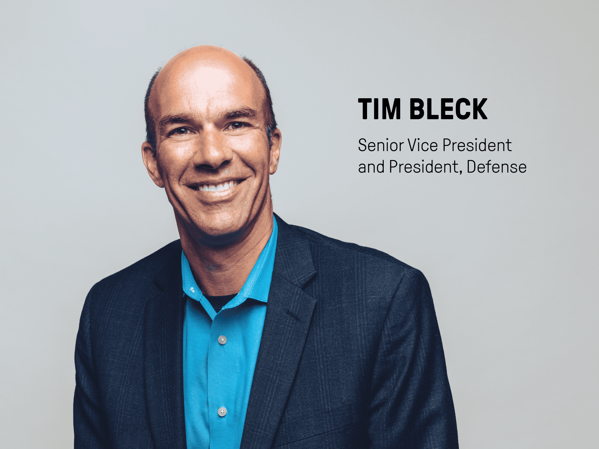 Tim Bleck wearing black suit jacket with blue shirt with a grey background